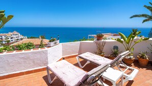 Eine Terrasse mit zwei Liegestühlen und Topfpflanzen, mit Blick auf die Küste.