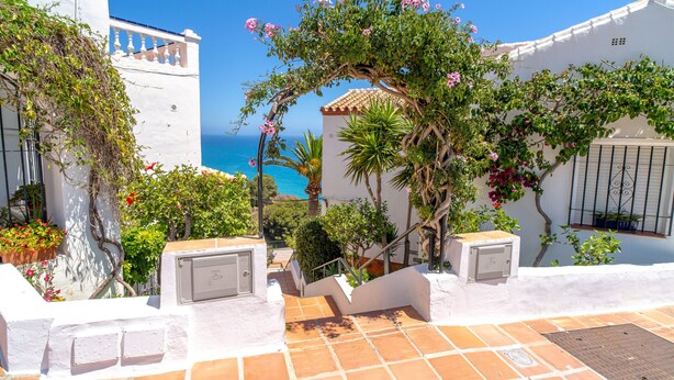 Ein weißes Gebäude mit einer gefliesten Terrasse, einer Treppe und Blick aufs Meer.