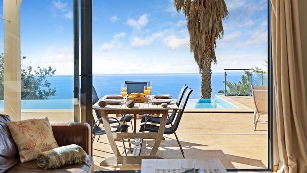 A room with a view of the sea, a dining table with chairs, a sofa, and a large window. - 17°West – Holiday villa (option with heated pool) (Estreito da Calheta)
