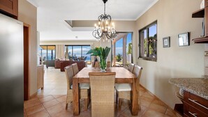 A spacious dining area with a large wooden table and wicker chairs, a chandelier, and a view of the ocean. - 17°West – Holiday villa (option with heated pool) (Estreito da Calheta)