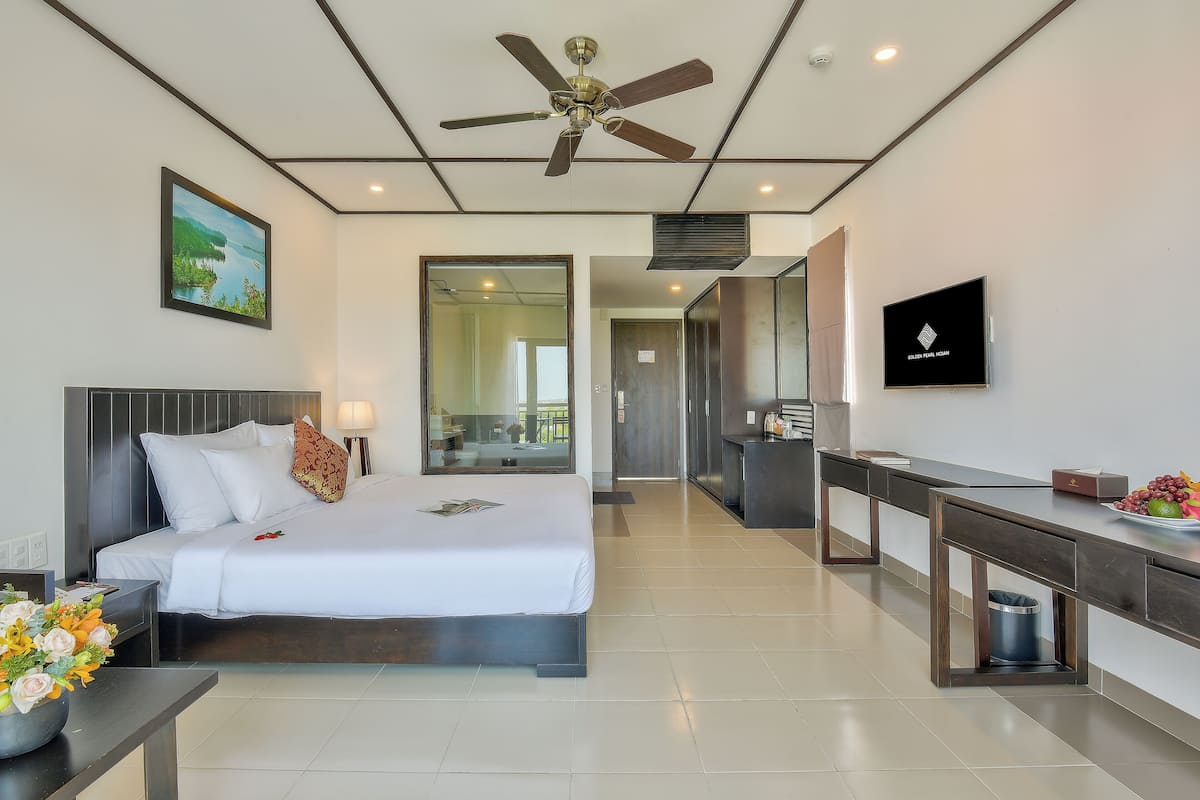 A modern hotel room with a bed, a desk, a TV, and a ceiling fan.