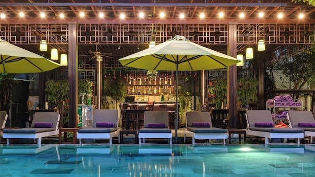 Zona de piscina con sillones de descanso y sombrillas, un bar con estantes llenos de botellas y un techo decorativo.