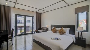 Habitación de hotel con una cama grande, un escritorio, una silla, una ventana con cortinas y un balcón.