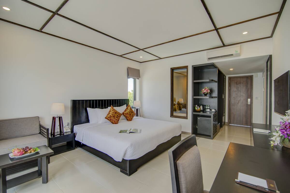 A modern hotel room with a large bed, bedside tables, a desk, and a seating area.
