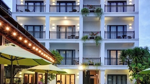 Un hotel de varios pisos con piscina, asientos exteriores y balcones con plantas.