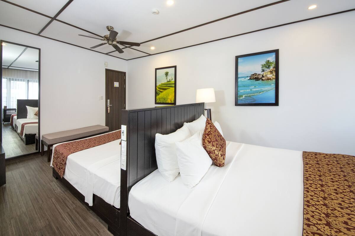 A hotel room with two single beds, a desk, a chair, a ceiling fan, and a large mirror.