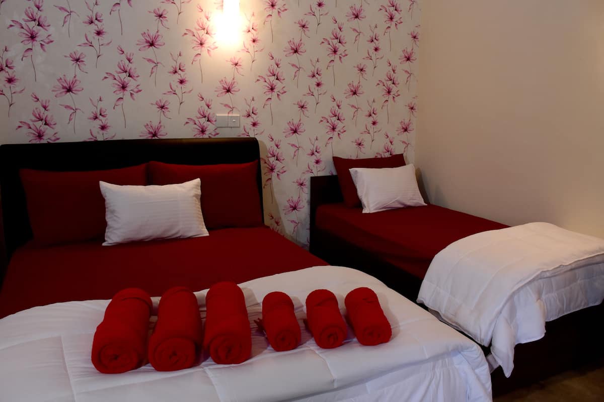A hotel room with two beds, red bedding, white pillows, and a floral wallpaper.