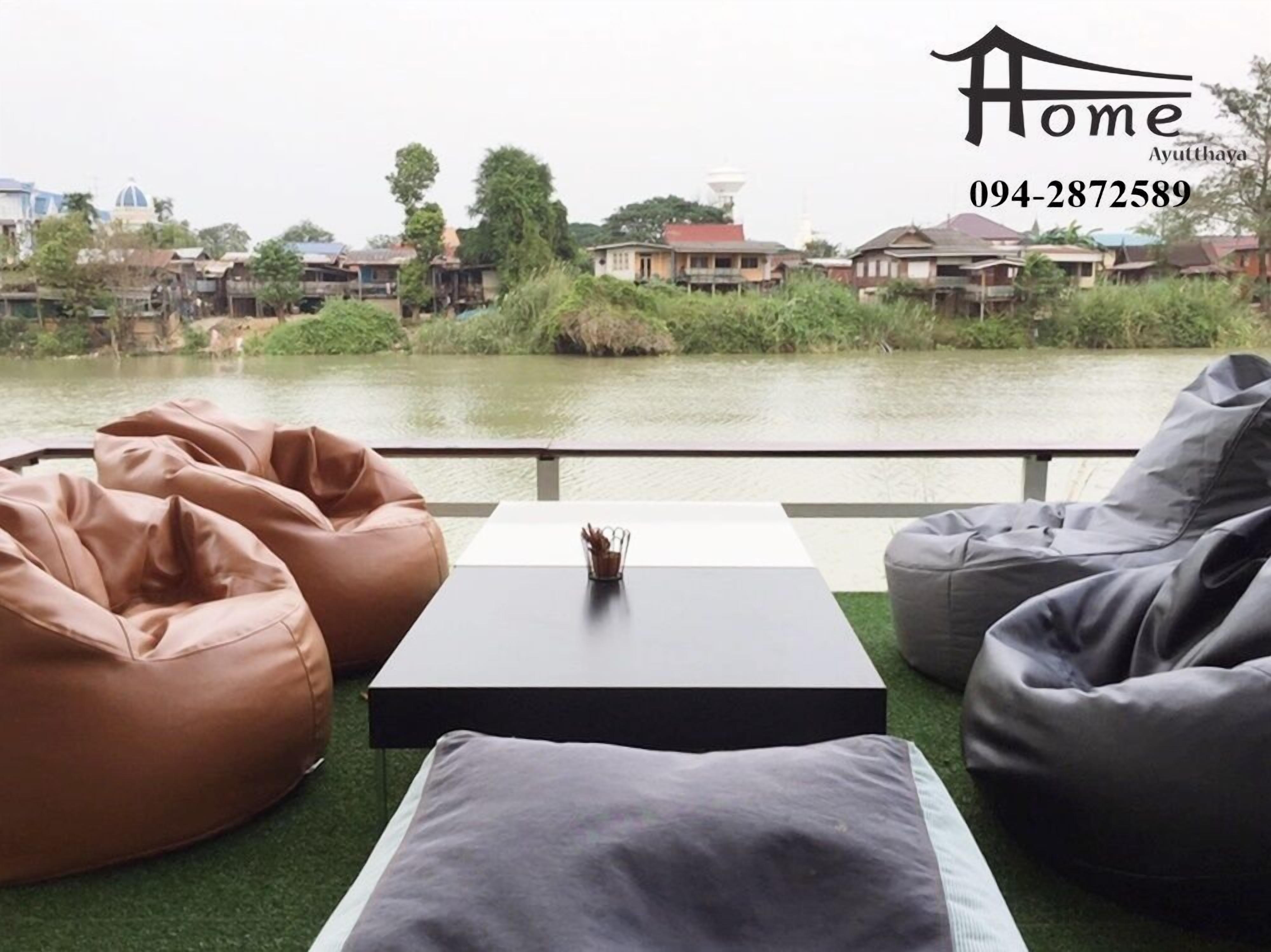 A view from a balcony with bean bags and a table, overlooking a river with houses in the background.