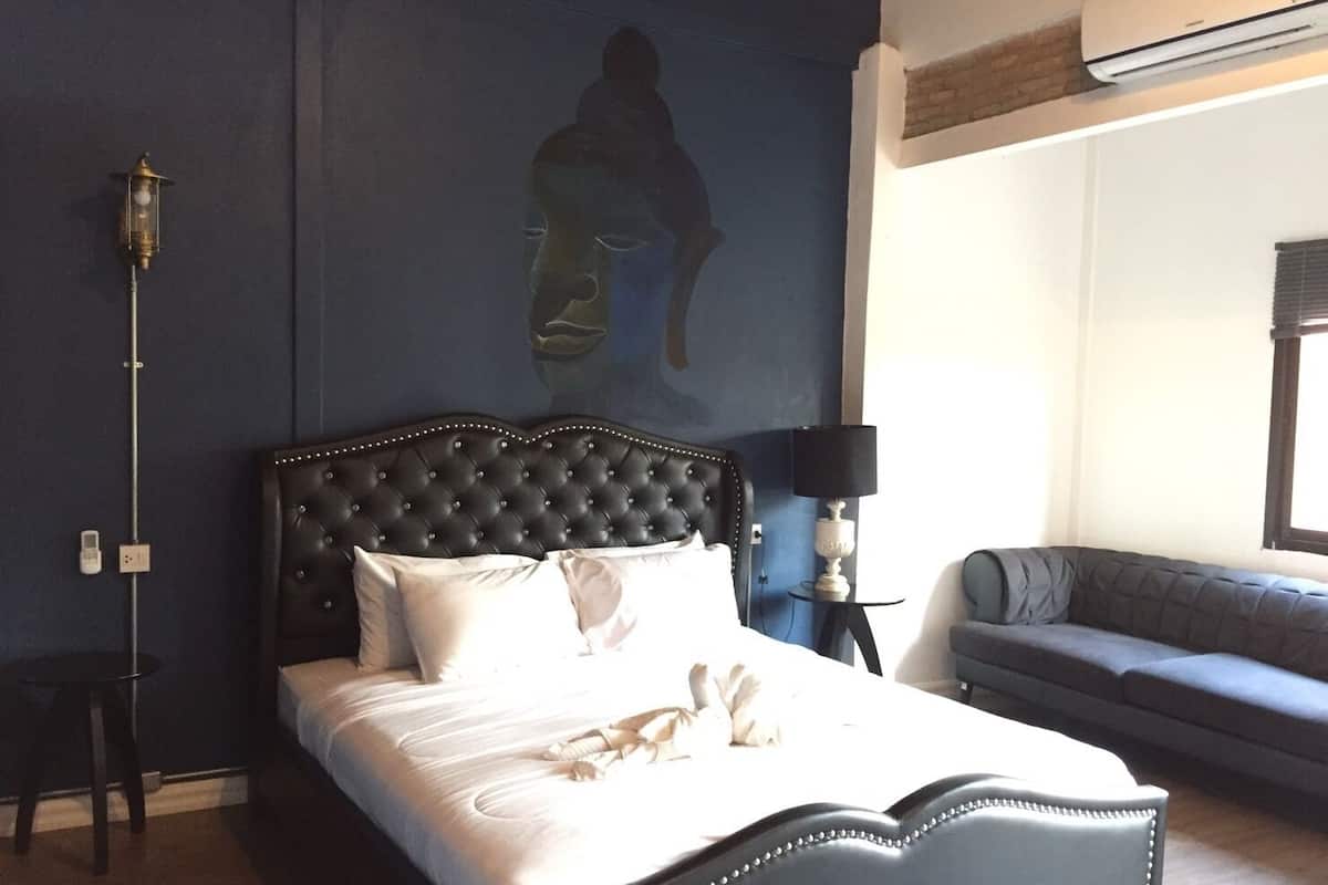A hotel room with a large bed, a sofa, a wall-mounted air conditioner, and a wall-mounted lamp.