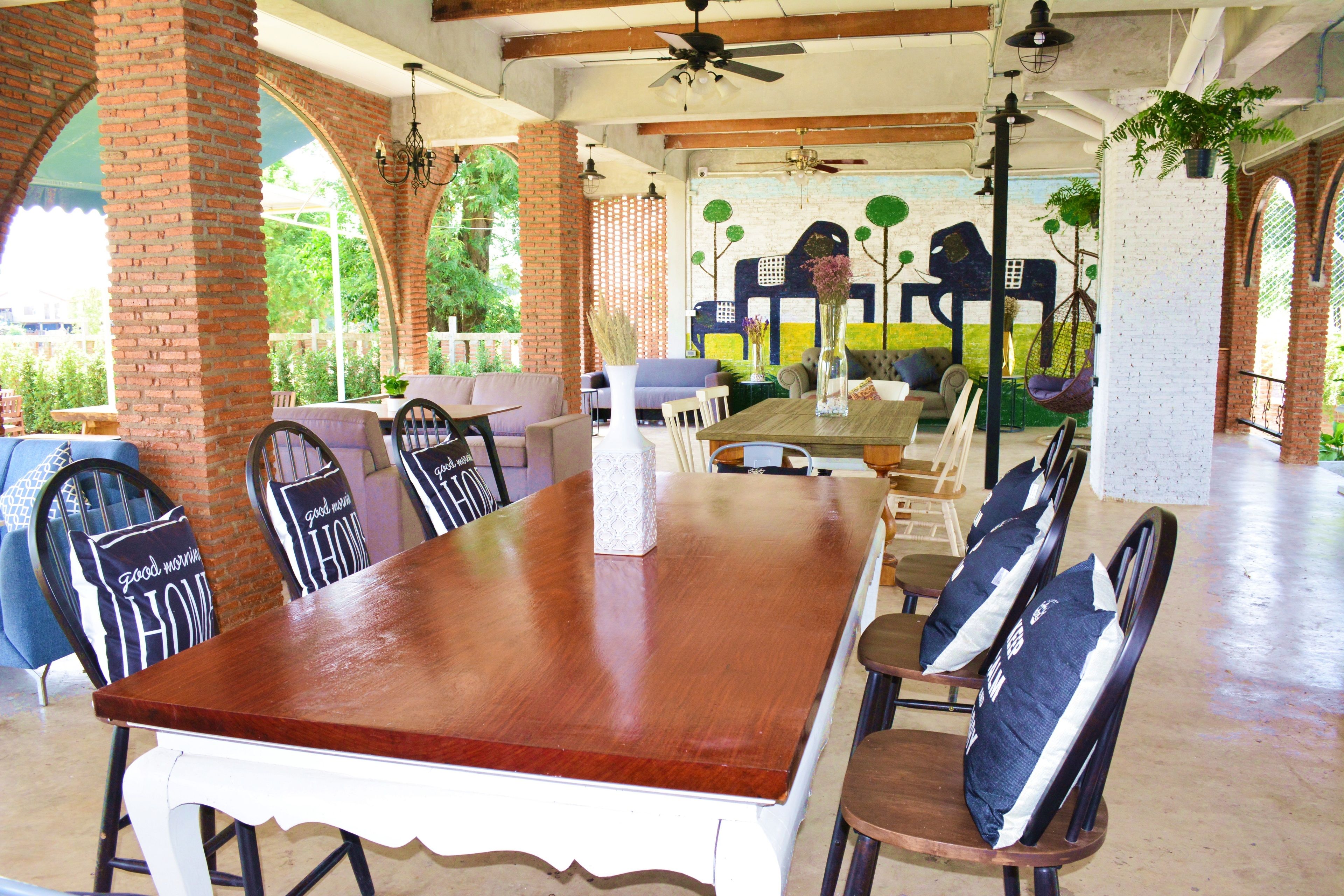 A spacious dining area with a long wooden table and multiple chairs, featuring a brick wall and large windows.