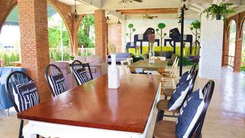 A spacious dining area with a long wooden table and multiple chairs, featuring a brick wall and large windows.