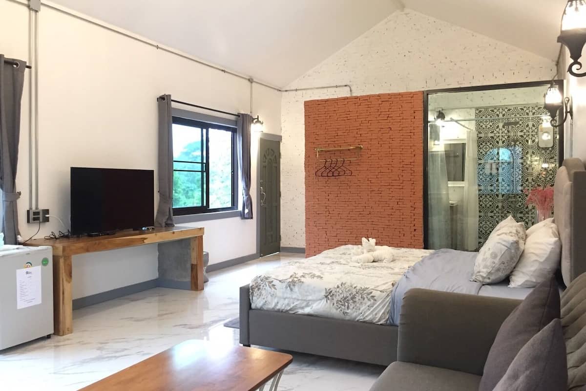 A modern bedroom with a bed, a sofa, a TV, and a window with curtains.