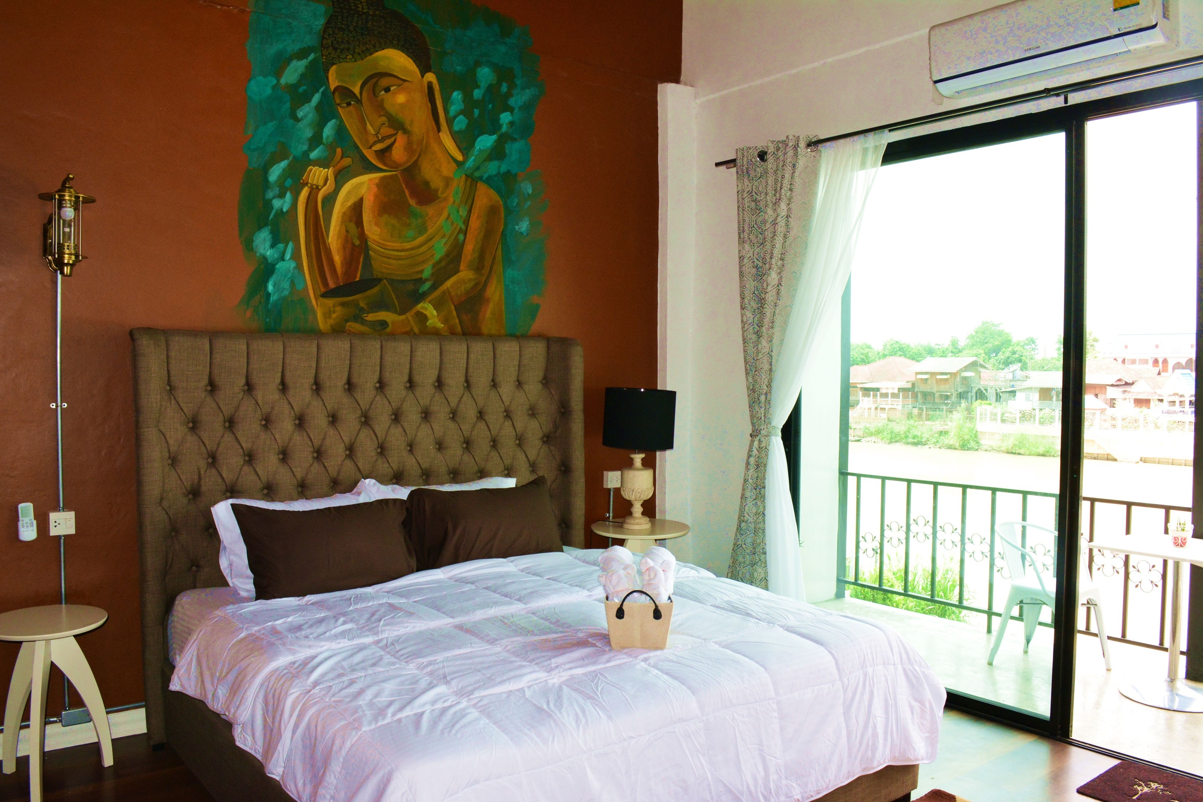 A bedroom with a large bed, a Buddha mural, a window with a view, and a small table.