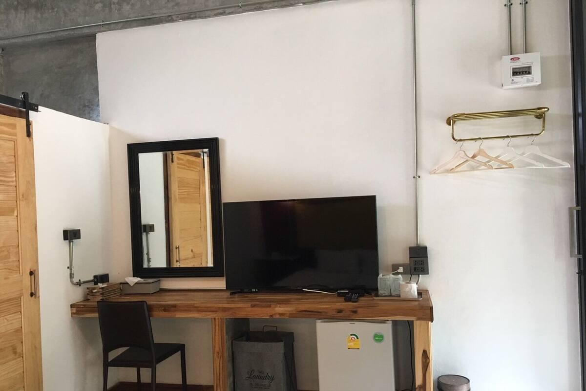 Une pièce de taille modeste, avec un bureau en bois, un téléviseur noir, un petit réfrigérateur et un miroir au mur.