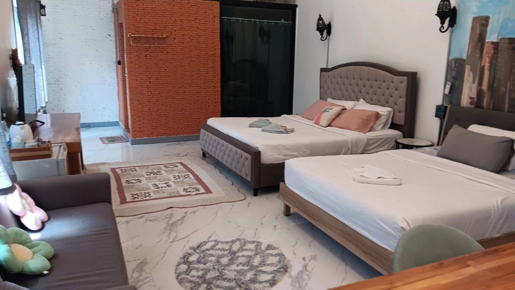 Quarto de hotel com duas camas, um sofá, uma mesa pequena e um tapete decorativo.
