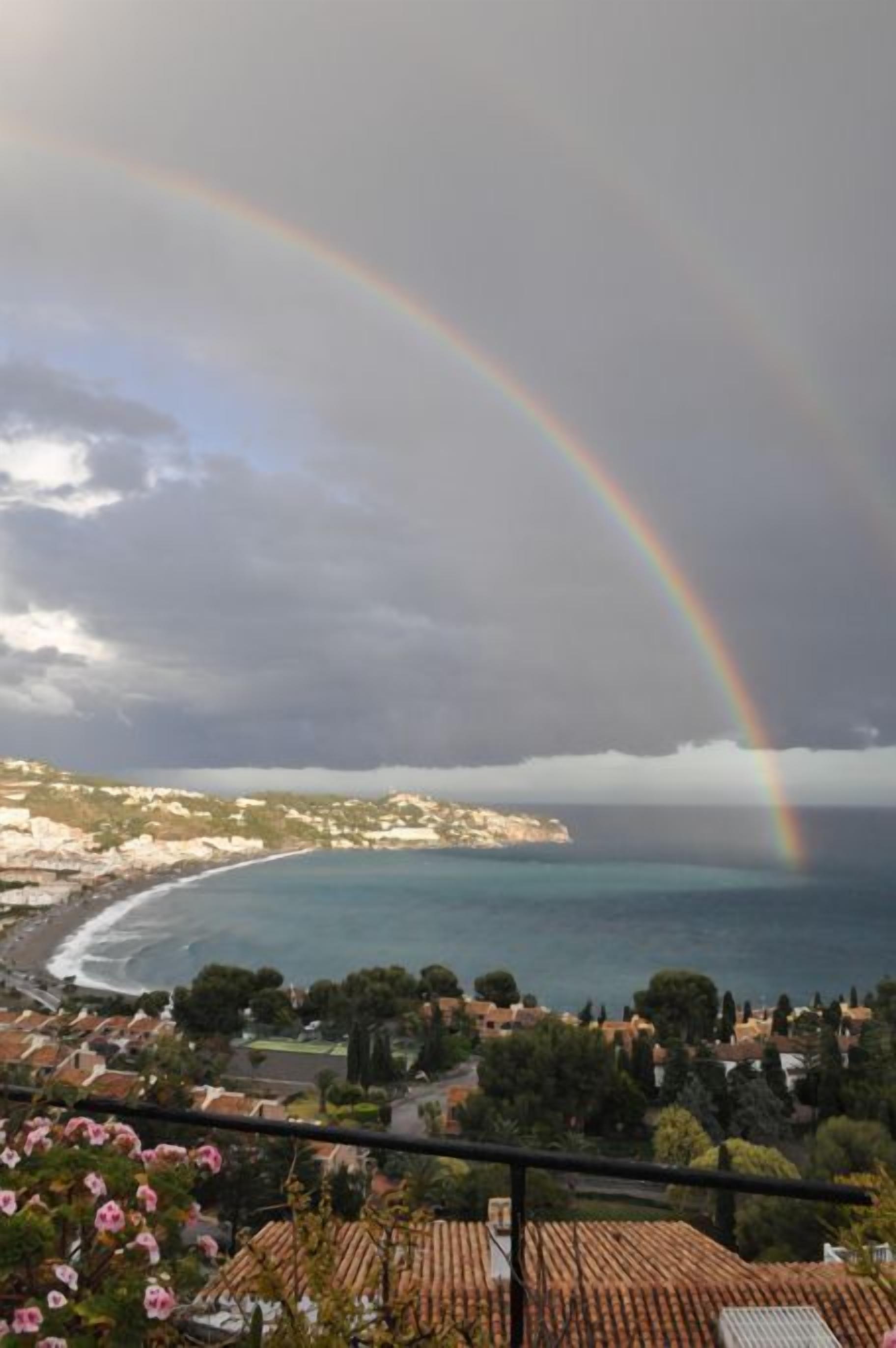 A coastal view with a rainbow, houses, and a beach.