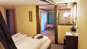 A bedroom with a bed, a bedside table, a mirror, and a door leading to another room. - Cozy half-timbered house for large groups / families up to 17 persons (Bacharach)