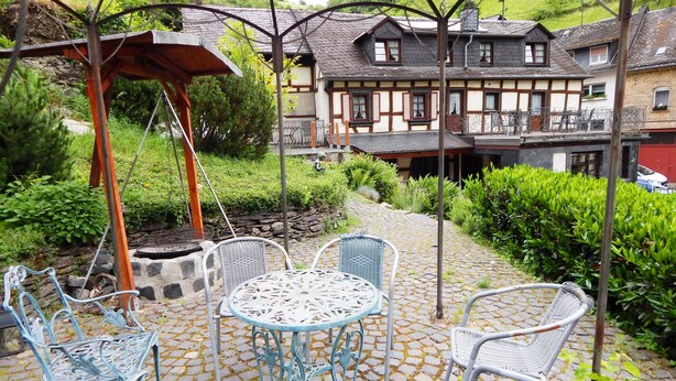 A courtyard with a stone-paved patio, wicker chairs, and a metal table. - Cozy half-timbered house for large groups / families up to 17 persons (Bacharach)