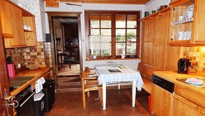 A cozy kitchen with wooden cabinets, a dining table with chairs, and a window with a view of the outdoors. - Cozy half-timbered house for large groups / families up to 17 persons (Bacharach)