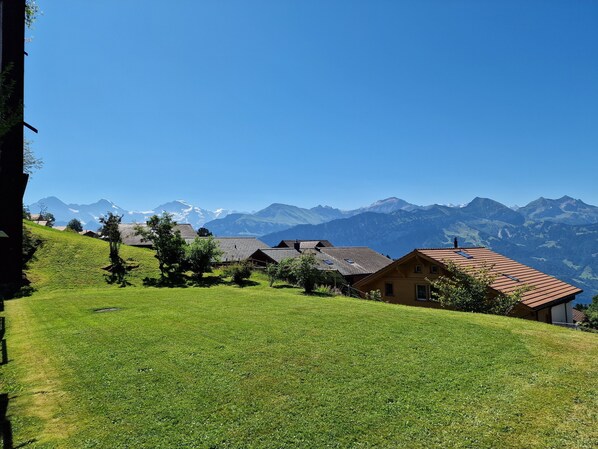 A rural village with traditional houses, a grassy hill, and a mountain range in the background. - Beatenberg, large, quiet 1 room apartment Wi-Fi / WLAN, balcony, view (Beatenberg)