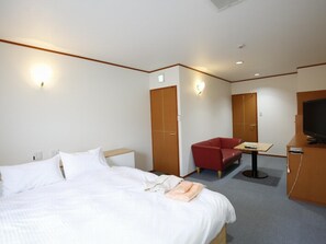 A hotel room with a bed, a red chair, a small table, a TV, and a wardrobe.