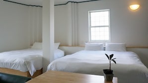 Une chambre d’hôtel avec deux lits, une fenêtre laissant entrer la lumière naturelle, une table de chevet et une plante en pot.