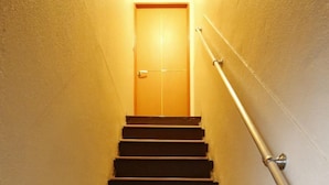 Un escalier avec des marches en bois et une rampe métallique, menant à une porte fermée en haut.