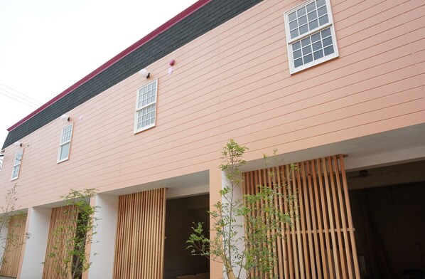 A two-story building with a pink facade, multiple windows, and wooden slats on the ground floor.