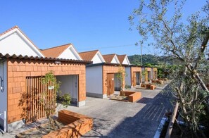 Una hilera de edificios modernos de una sola planta con fachadas de ladrillo y techos de tejas, ubicados a lo largo de un sendero pavimentado con jardineras de madera y pequeños árboles.