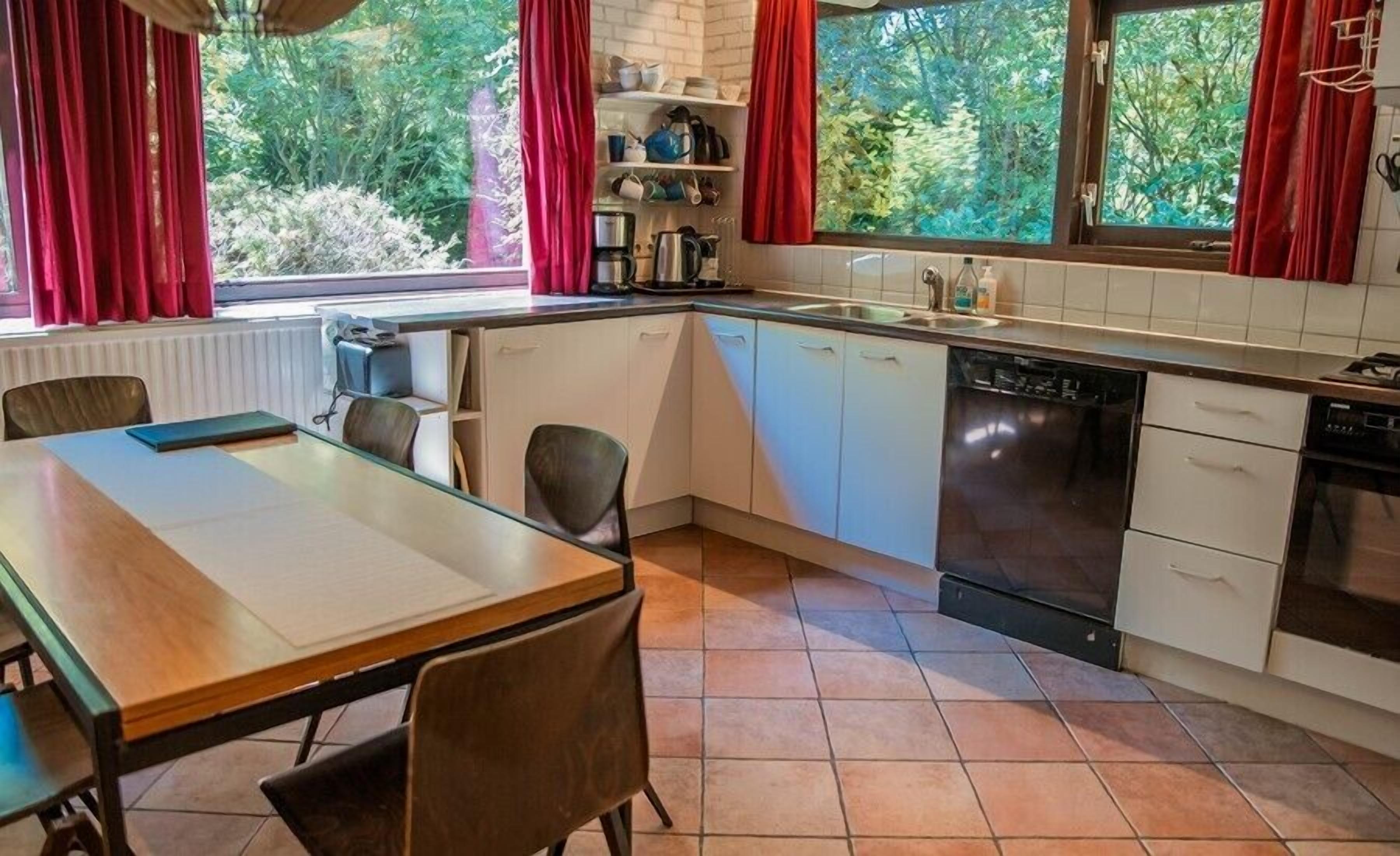 Eine kleine Küche mit weißen Schränken, einem Geschirrspüler und einem Fenster mit roten Vorhängen.