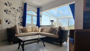 A modern living room with a beige sectional sofa, a glass coffee table, and wicker chairs.