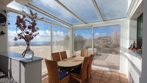 A sunroom with a dining table, chairs, and a vase of flowers.