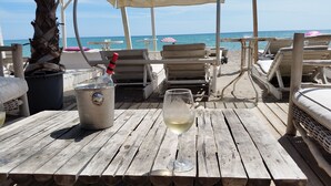 A wooden deck with a table, a bottle of champagne, and a glass of white wine.