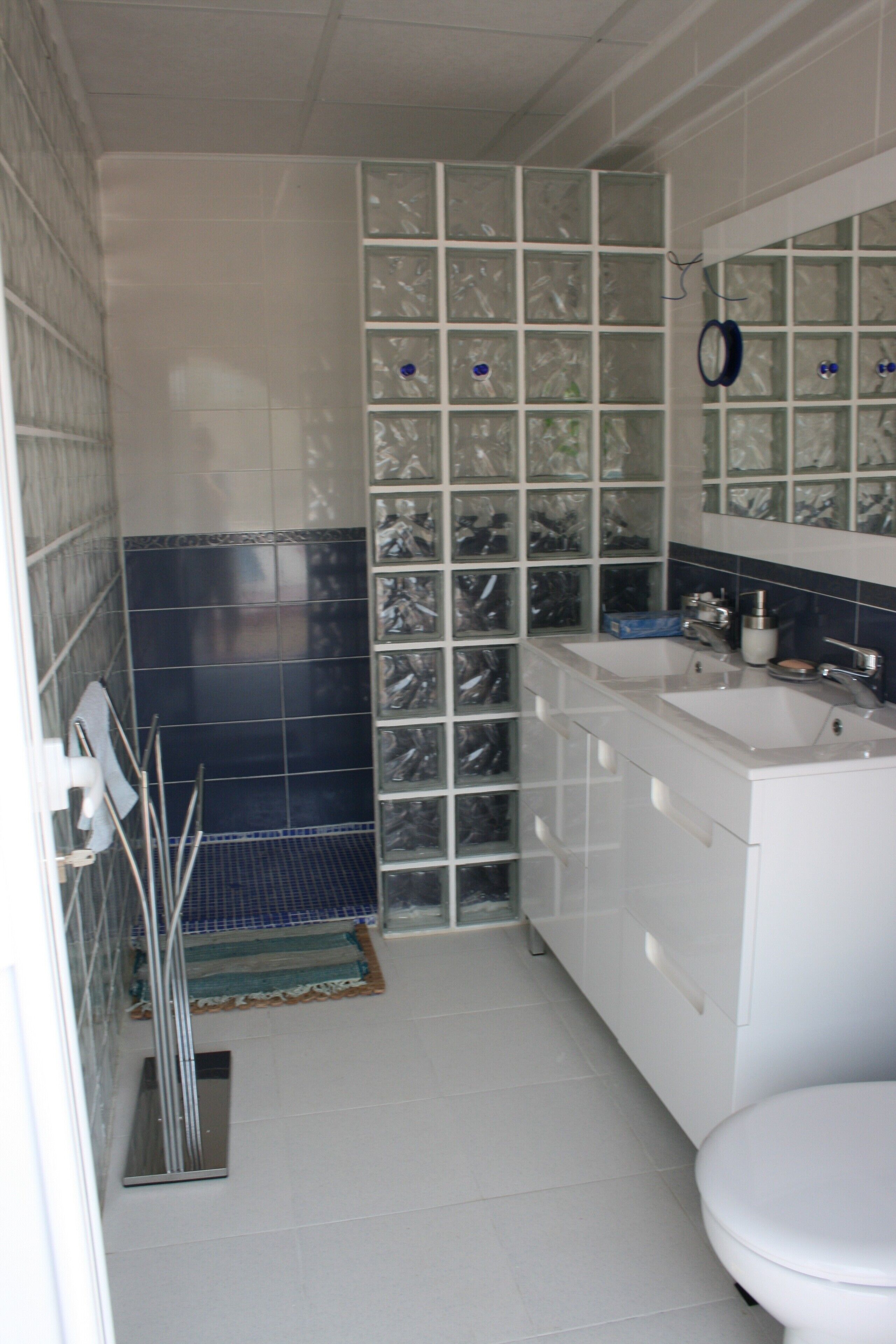 Ein Badezimmer mit weißem Waschbecken, Spiegel und Toilette. Eine blaue Fliesenwand und eine Glasbaustraße sind vorhanden.