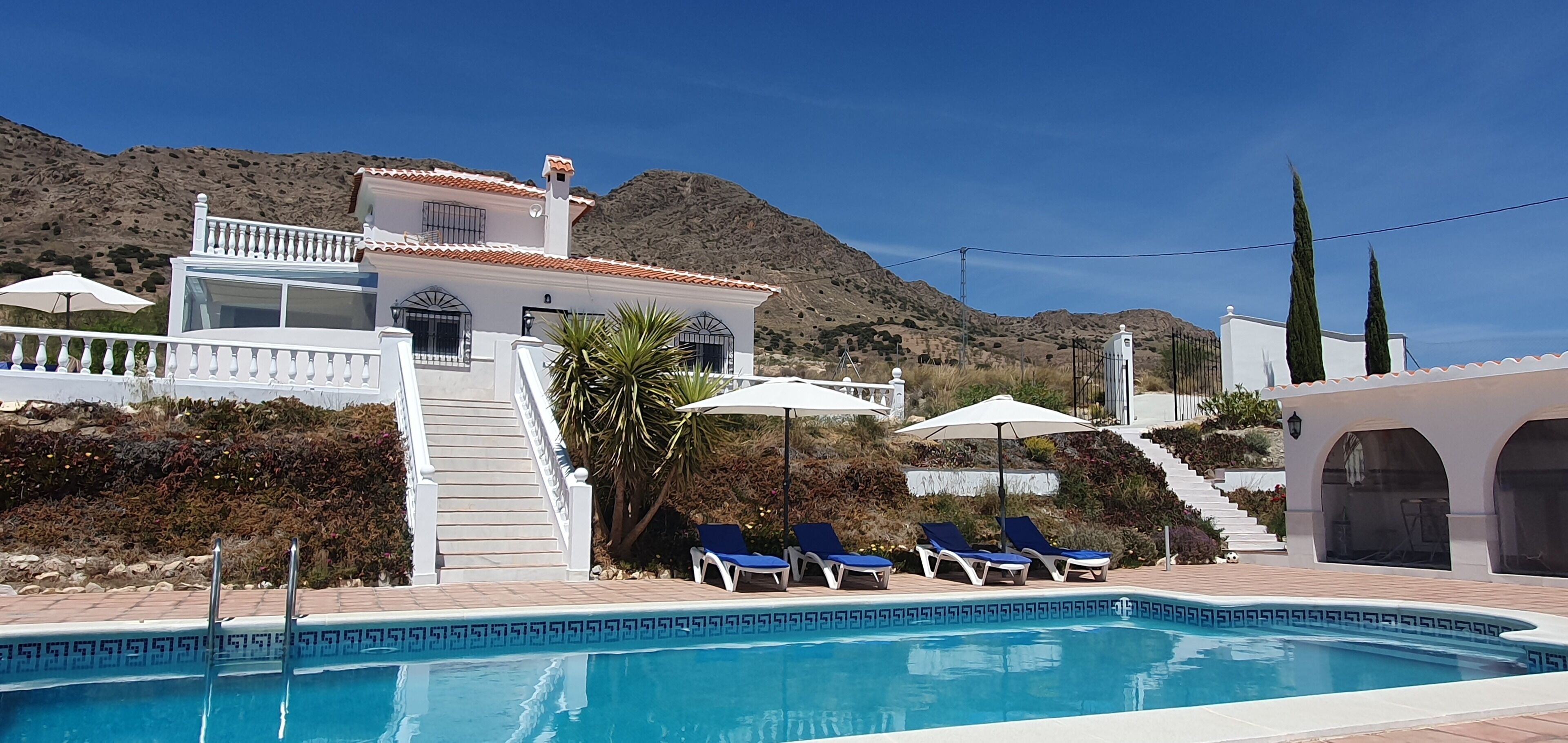 Uma área de piscina com vista clara para a piscina, uma escadaria que leva a um edifício e uma montanha ao fundo.
