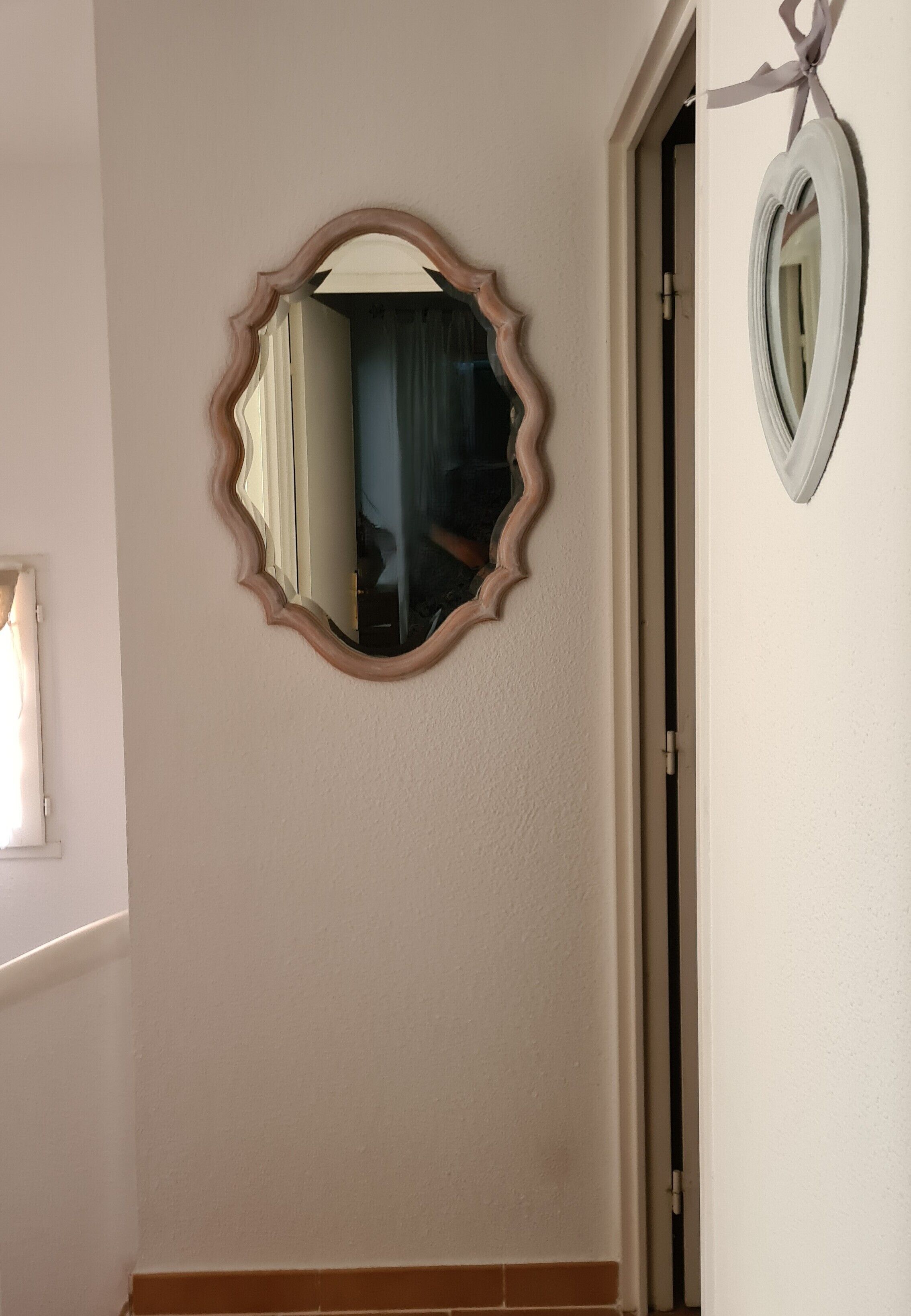 Una habitación con un espejo grande en la pared, una puerta y una ventana con cortinas.