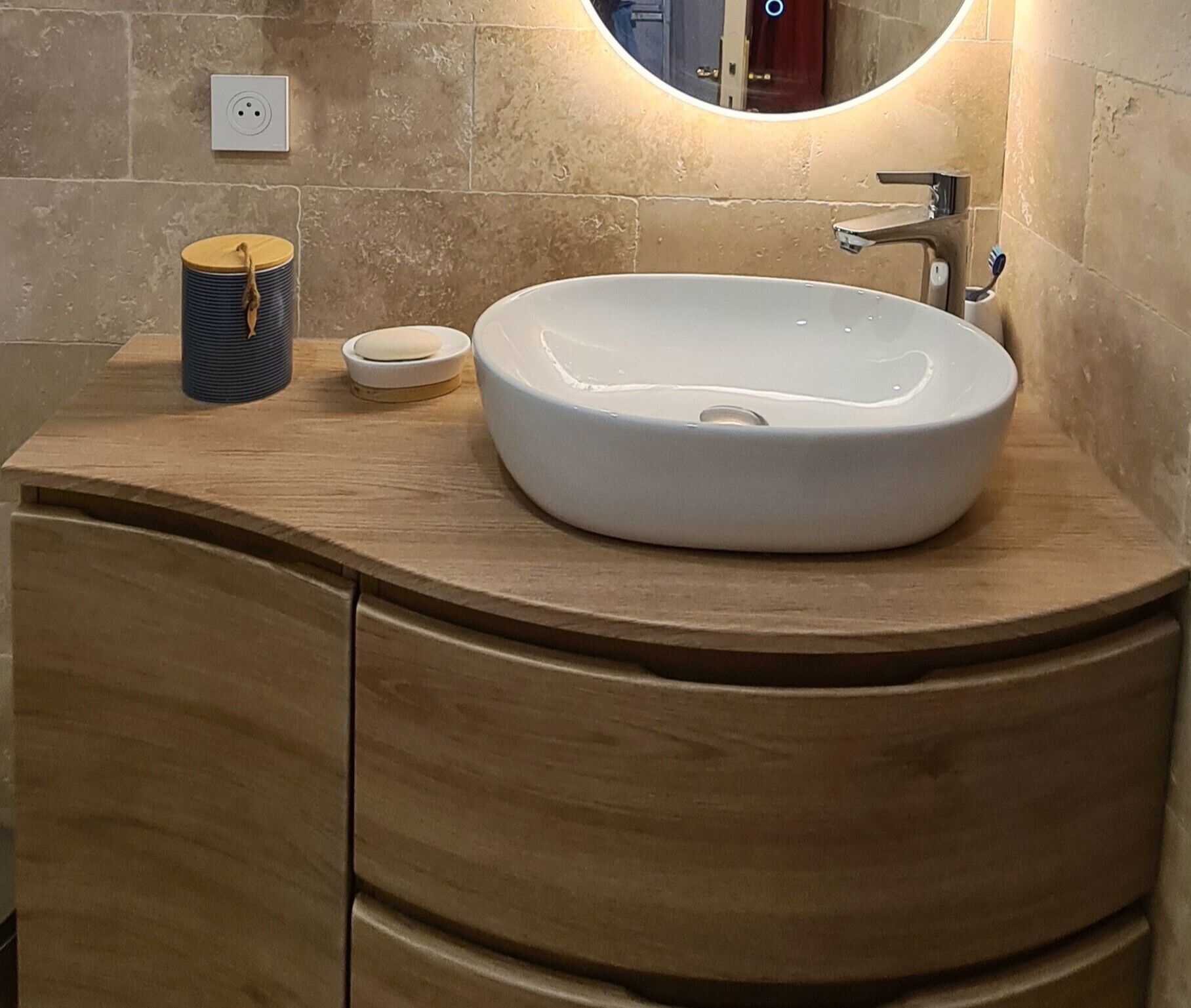 Une salle de bain avec un lavabo rond blanc, un miroir et un meuble-lavabo en bois.