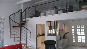 A spacious living area with a curved staircase, a kitchen, and a seating area with a red sofa. - Saint Aubin de Médoc will take place from August 22 to 29, 2026 (Saint-Aubin-De-Médoc)