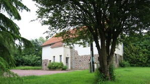 A white building with a red-tiled roof, surrounded by lush greenery and a gravel path. - Family-friendly with pets allowed and WiFi (Cérences)