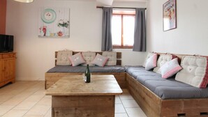 A cozy living room with a wooden coffee table, a sofa with patterned cushions, a television, and a window with curtains. - Family-friendly with pets allowed and WiFi (Cérences)