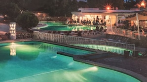 Una piscina con zona a basso livello, sdraio e un'area salotto coperta con persone.