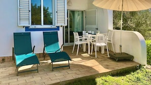 Un patio con tavolo e sedie, un ombrellone grande e una porta scorrevole che dà su uno spazio interno.