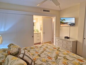 Une chambre à coucher comprenant un lit, une commode, un téléviseur et une porte donnant sur une salle de bain.