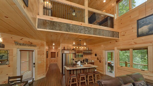 A cabin interior with a dining area, kitchen, and a loft bedroom.
