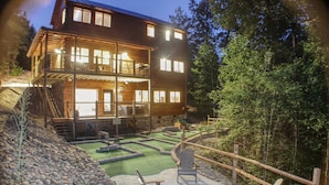 A two-story wooden building with a covered outdoor area featuring a fire pit, seating, and a small pool.