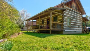 A log cabin with a porch and a covered deck, surrounded by a grassy yard and trees. - Creekside Bliss! Back Yard Creekside Retreat !!! (Cosby)