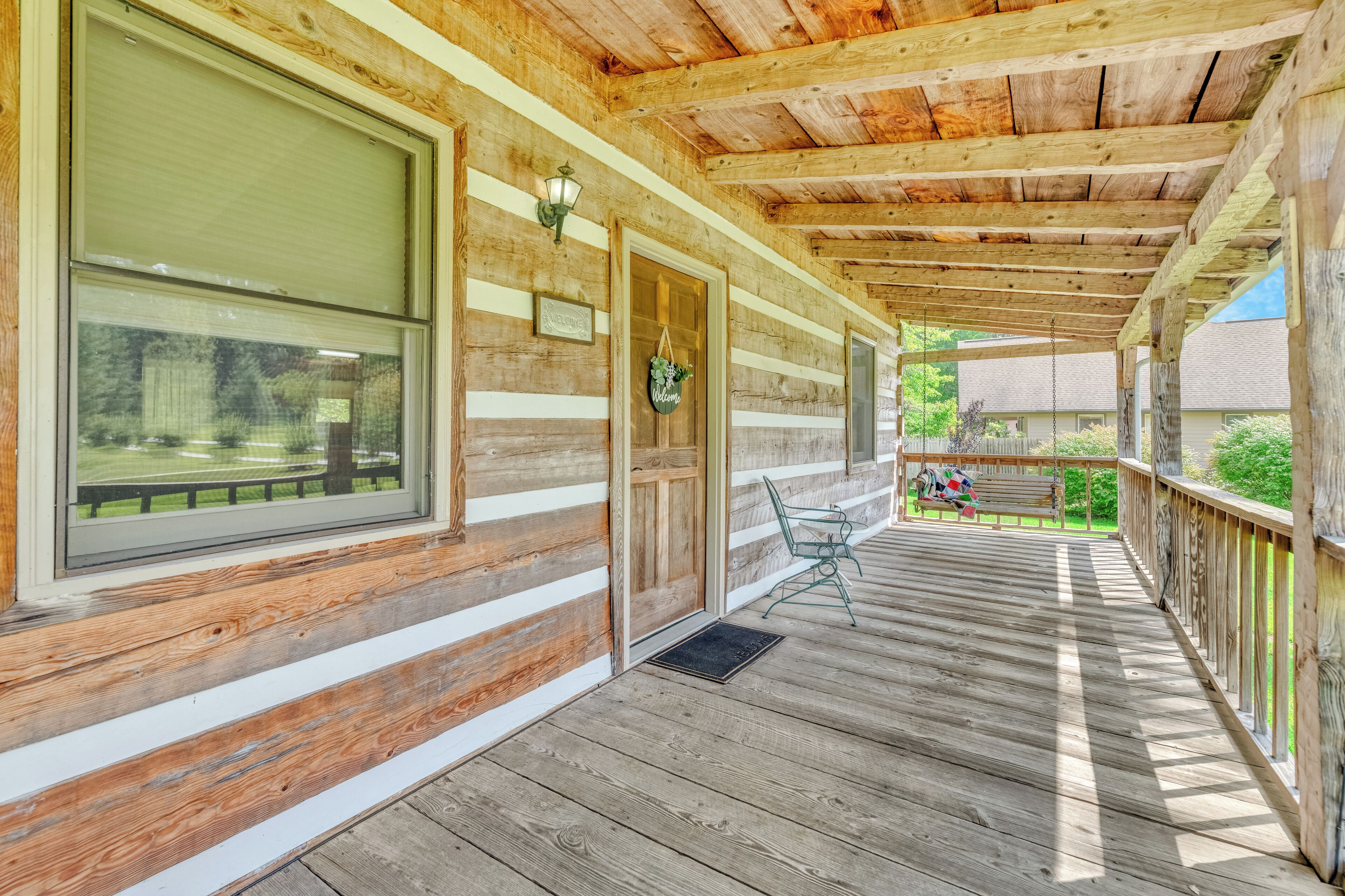 A wooden cabin with a covered porch, large windows, and a door with a hanging decoration.