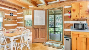 A cabin interior with a wooden dining table and chairs, a wooden door, a microwave, and a small refrigerator. - Creekside Bliss! Back Yard Creekside Retreat !!! (Cosby)