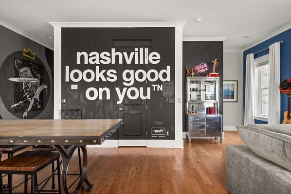 Un salon moderne avec un grand mur noir orné d’une citation inspirante, une table à manger en bois et un canapé gris.