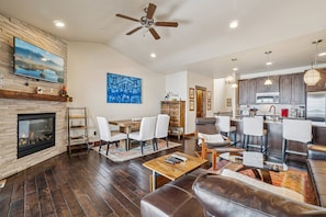 A spacious living area with a fireplace, a dining table, and a kitchen in the background.